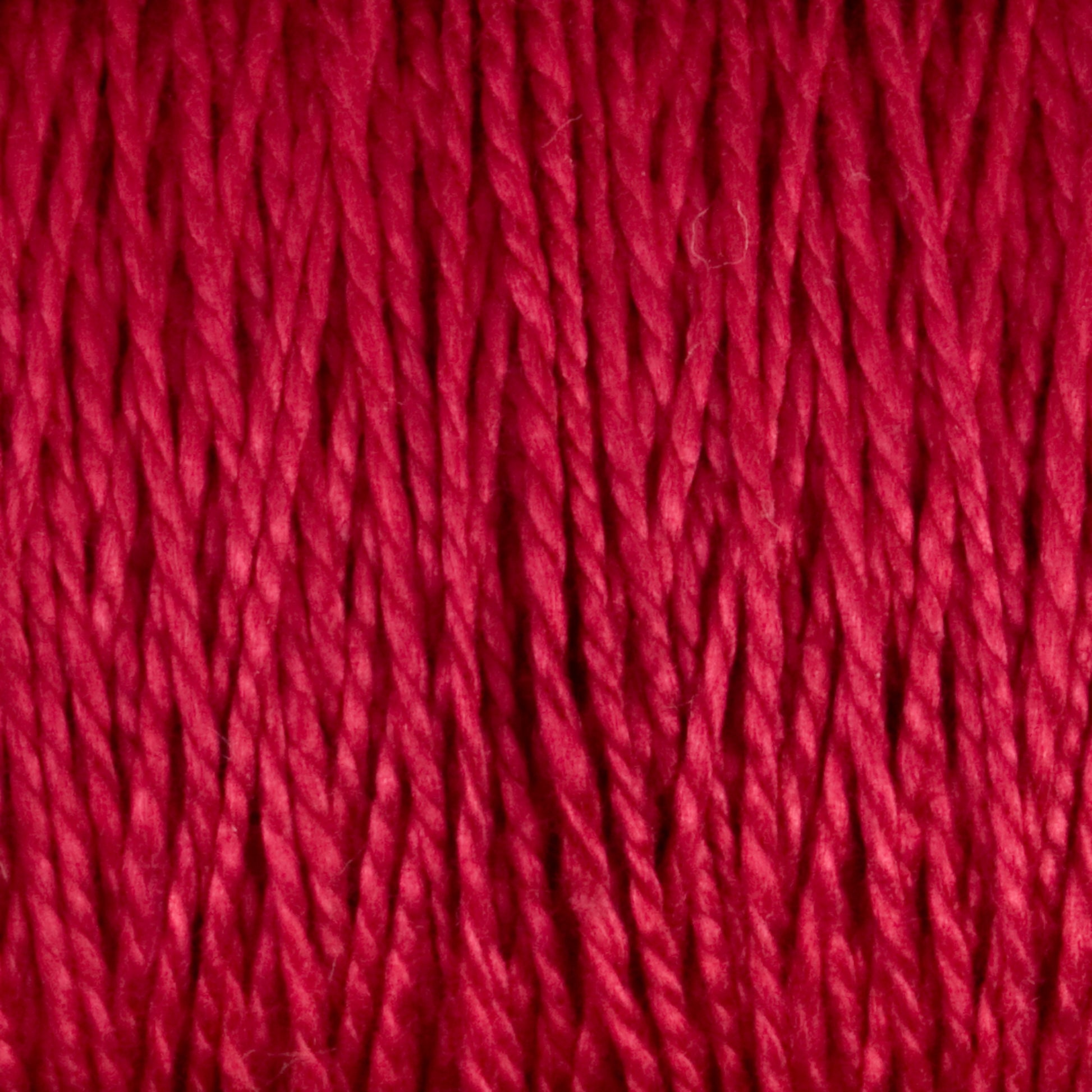 Close-up image of the 3/2 Pearl Cotton Yarn | Mini-cone by Supreme Corp, showcasing tightly wound red strands with slight variations in thickness and a subtle sheen. The versatile yarn appears soft and vibrant, indicating richness in color and texture, suitable for knitting, crocheting, or other fiber arts projects.