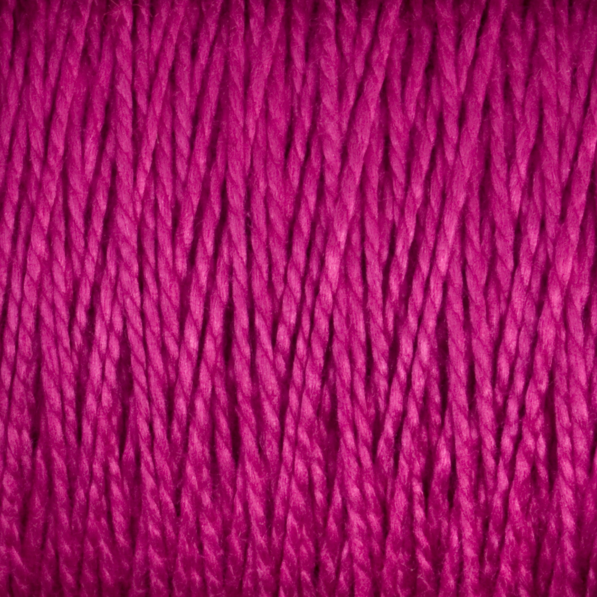 Close-up image of tightly wound, vibrant magenta 3/2 Pearl Cotton Yarn | Mini-cone from Supreme Corp. The texture of the versatile yarn is visible, showcasing individual fibers twisted together to form a thick, coarse strand. The image highlights the consistent, intertwined pattern of the yarn fibers.