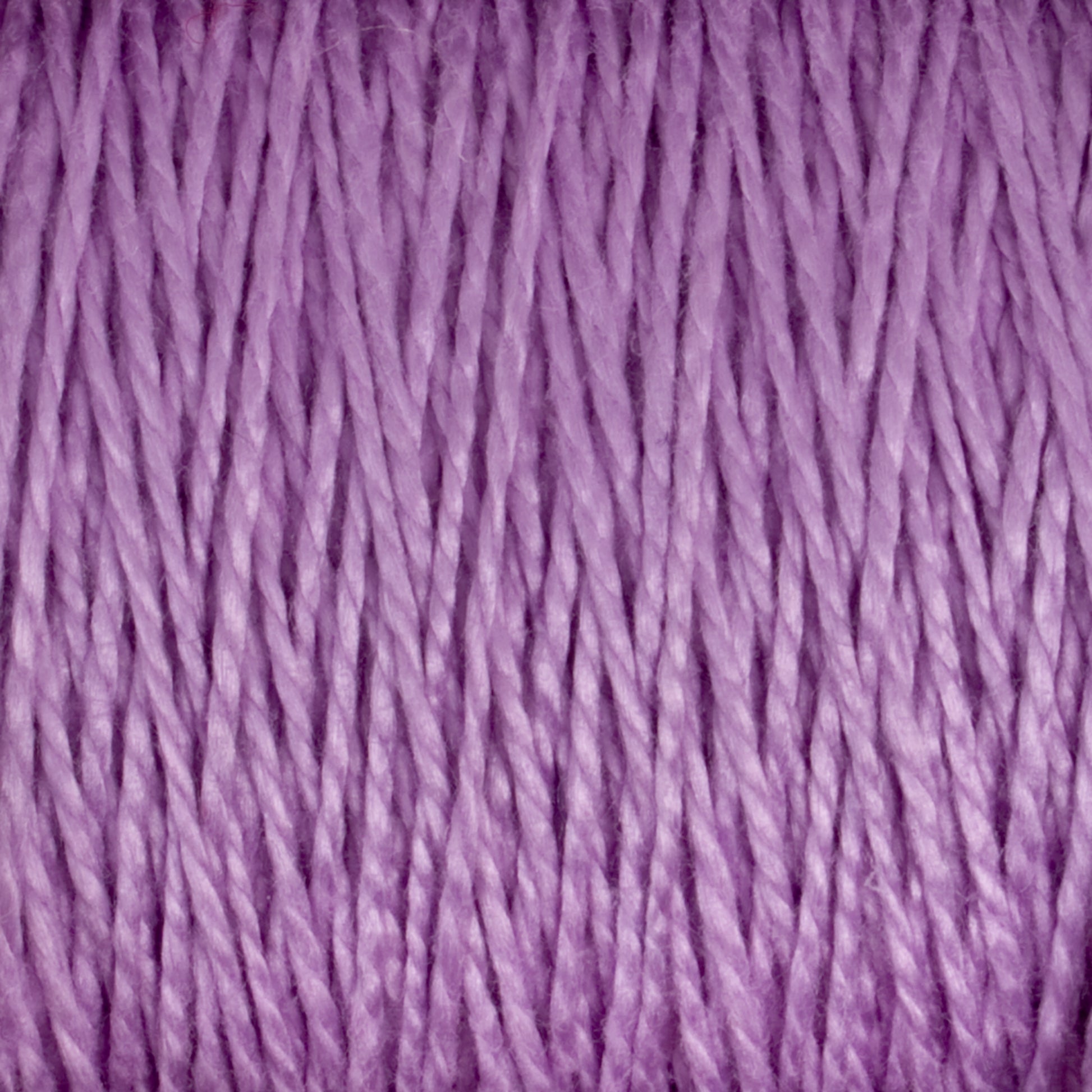 A detailed close-up of Supreme Corp's 3/2 Pearl Cotton Yarn in a lavender hue showcases its tightly twisted, mercerized fibers, resulting in a textured and soft appearance. This mini-cone of yarn highlights its consistent thickness and subtle sheen.