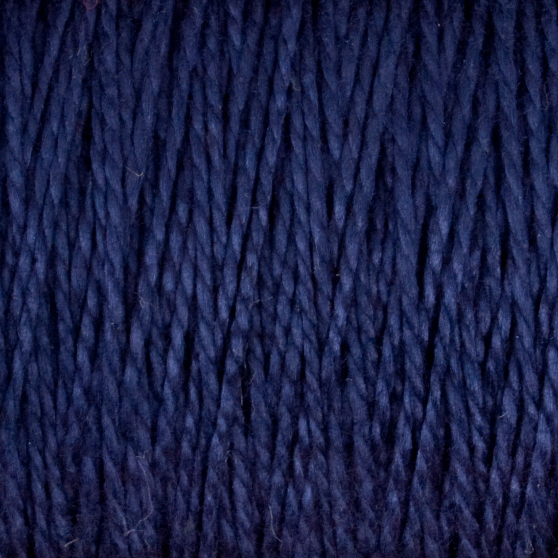 Close-up of tightly wound 3/2 Pearl Cotton Yarn from Supreme Corp, showcasing its textured, fibrous strands. This versatile mini-cone yarn appears soft and thick, with a rich, dark blue color that is consistent throughout.