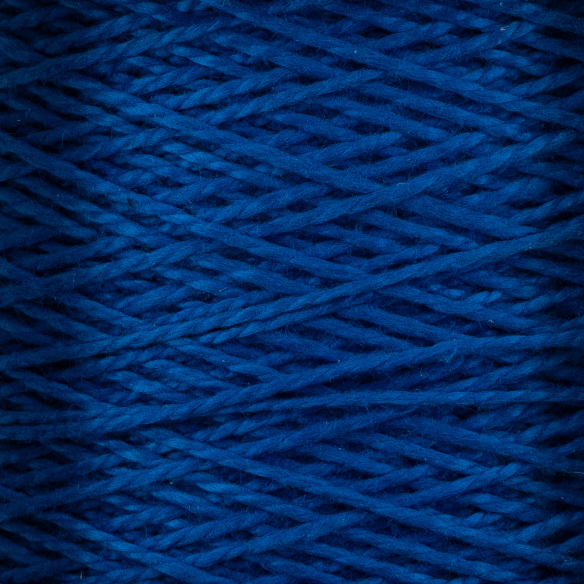 A close-up view of strands of Supreme Corp's 3/2 Pearl Cotton Yarn Mini-cone tightly wound together reveals a dense and textured pattern. The vibrant hue of the pearl cotton yarn is consistent throughout the image, showcasing the intricately intertwined threads and their fine details.