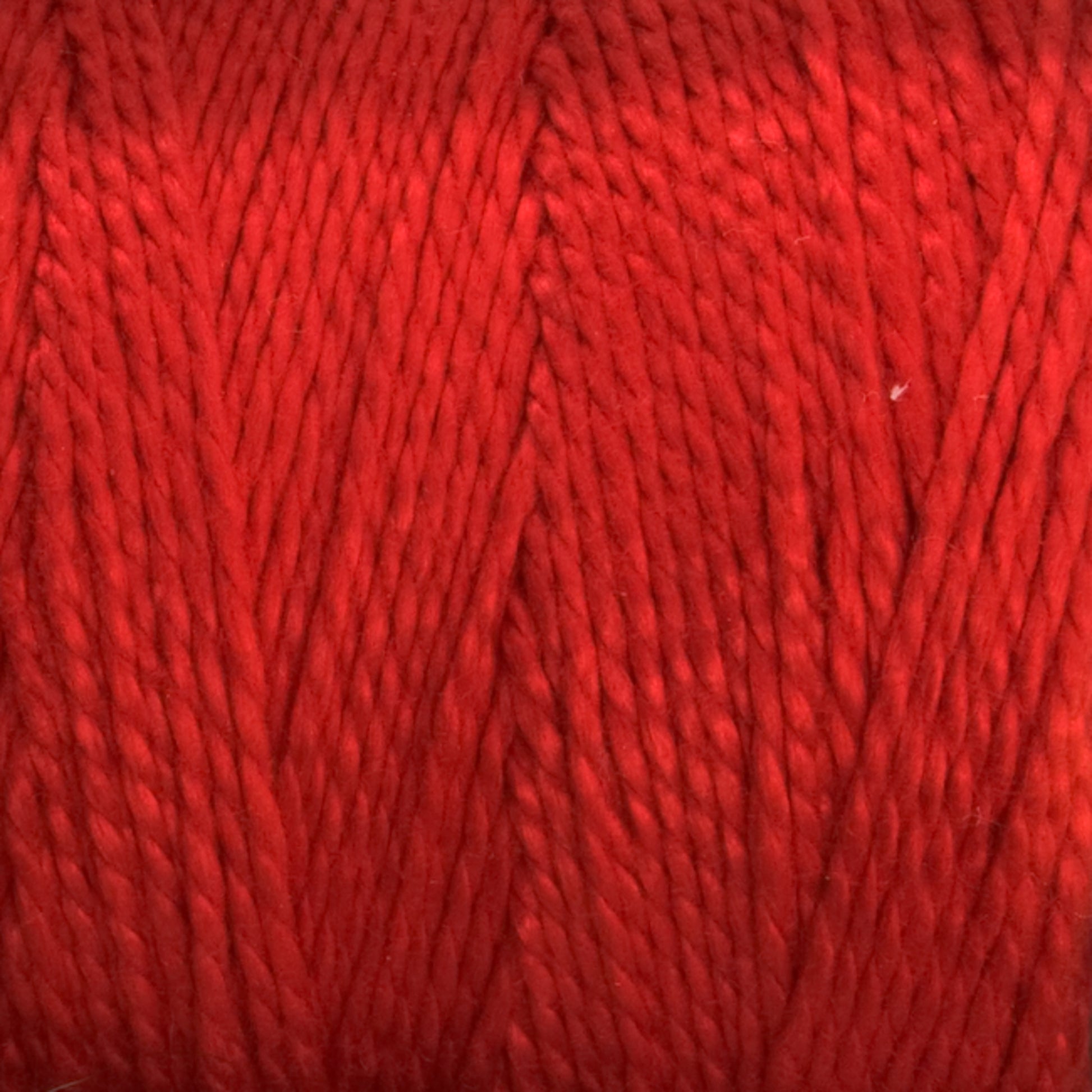 A close-up image of the soft, Supreme Corp 3/2 Pearl Cotton Yarn in a mini-cone format. The image highlights the smooth, finely twisted fibers, showcasing the texture and evenness of the yarn. The vibrant red shade features slight variations in the thread, creating a dynamic appearance.