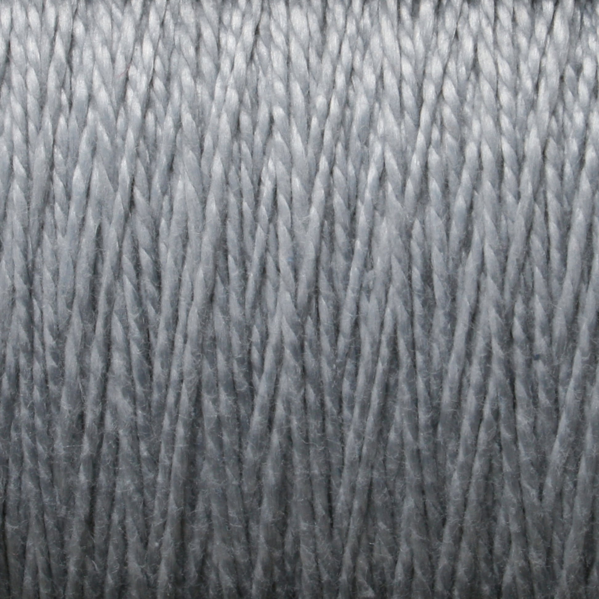 Close-up image of a mini-cone of Supreme Corp's 3/2 Pearl Cotton Yarn in gray, tightly wound in parallel layers, creating a textured pattern with visible strands. The image highlights the details of the mercerized cotton yarn's fibers and the uniformity of the winding.