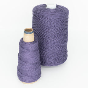 Two spools of versatile purple yarn from Supreme Corp are side by side on a white background. The larger spool, the 3/2 Pearl Cotton Yarn | Large Cone, is cylindrical and tall, while the smaller spool is cone-shaped.