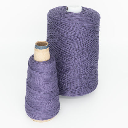 Two spools of versatile purple yarn from Supreme Corp are side by side on a white background. The larger spool, the 3/2 Pearl Cotton Yarn | Large Cone, is cylindrical and tall, while the smaller spool is cone-shaped.