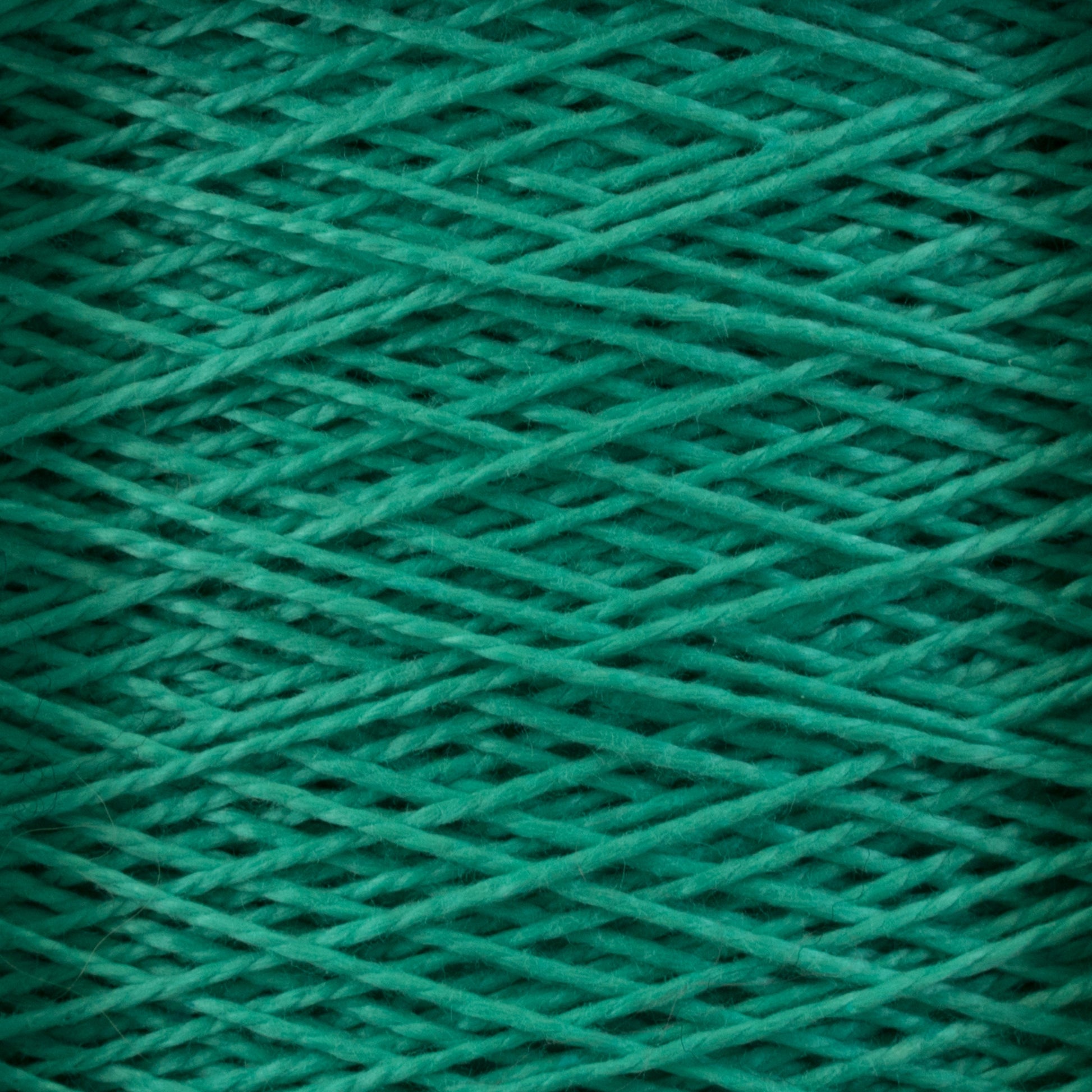 Close-up image of Supreme Corp's 5/2 Pearl Cotton Yarn wound tightly in overlapping layers, creating a textured pattern. The green yarn has a soft and slightly fuzzy appearance, giving the image a cozy and crafty feel—perfect for weaving projects.