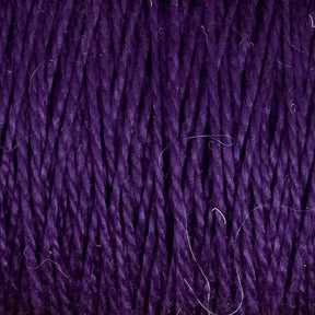 Close-up of Supreme Corp's 5/2 Pearl Cotton Yarn in a deep purple hue, ideal for weaving projects, with individual strands of fiber clearly visible. The texture is slightly fuzzy with a few loose fibers scattered on the surface, showcasing the yarn's unique characteristics on this mini-cone.