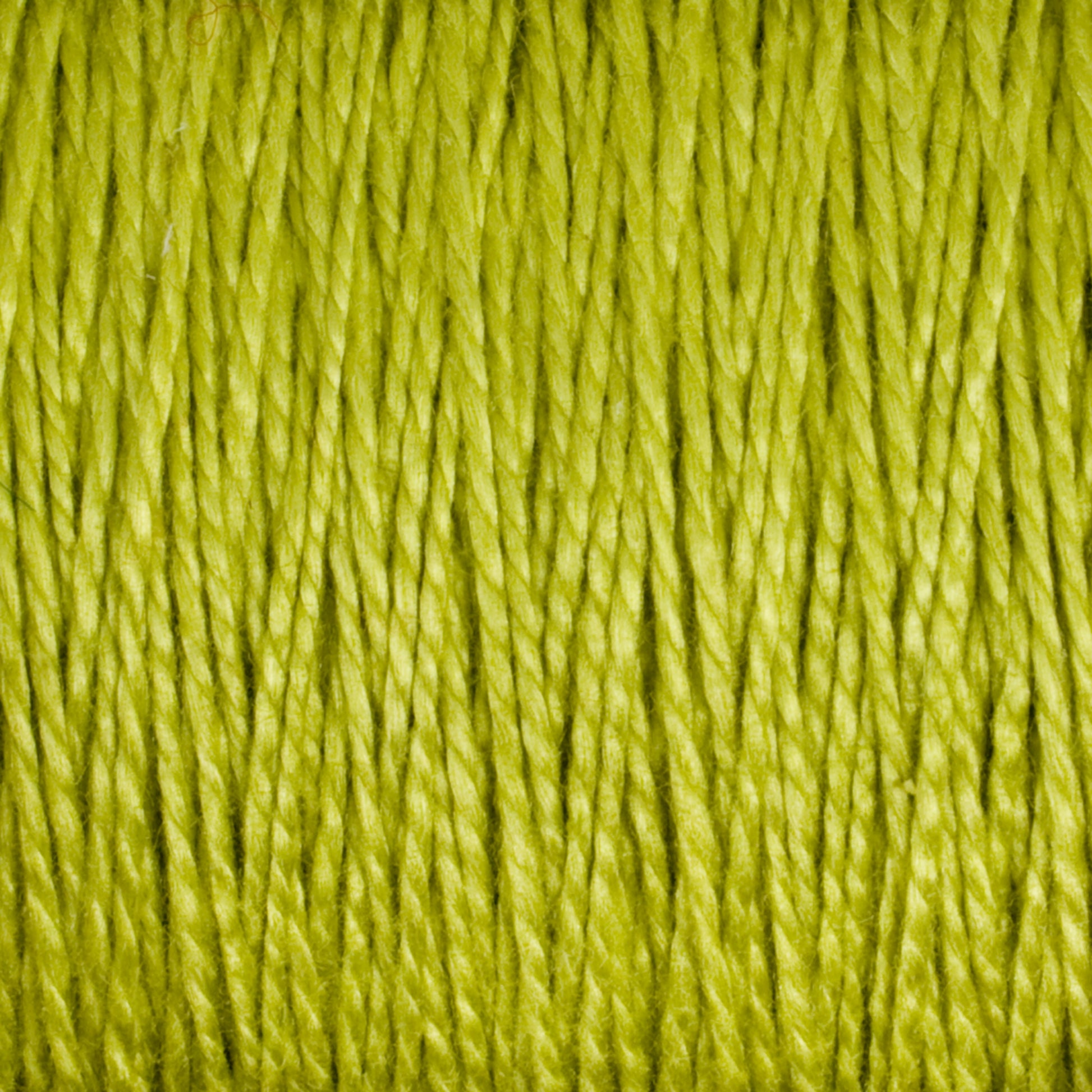 Close-up of Supreme Corp's 5/2 Pearl Cotton Yarn in green, showing tightly packed fibers with a slight sheen. The texture appears soft and smooth, with each strand clearly visible. The background is out of focus, emphasizing the intricacy of this versatile yarn's strands on the large cone.