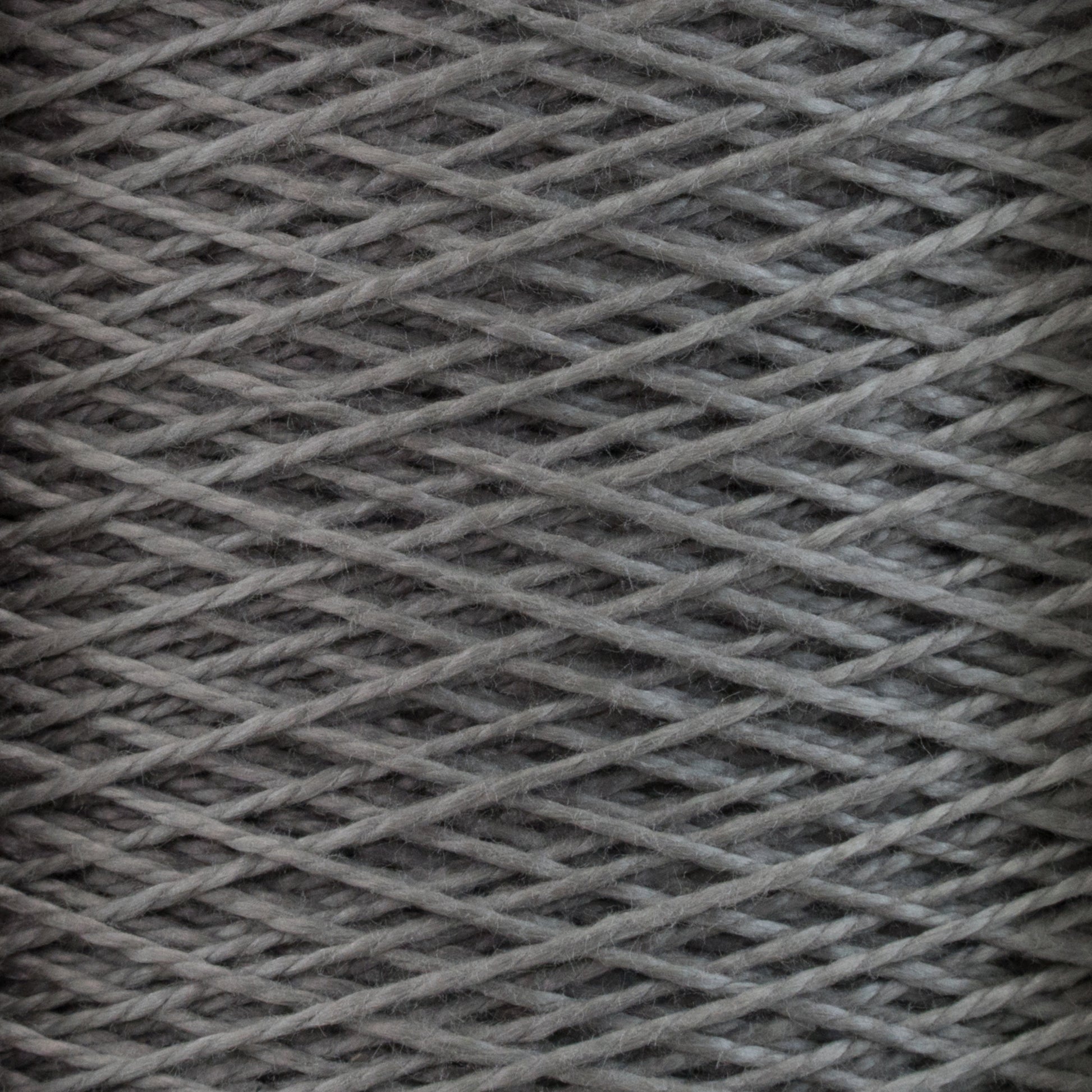 Close-up of a spool of gray 5/2 Pearl Cotton Yarn | Mini-cone by Supreme Corp, showcasing intricate crisscrossing threads wound tightly. The texture highlights the fibrous quality of the mercerized cotton yarn, ideal for weaving projects. The image emphasizes the pattern and texture of the material, perfect for detailed craftsmanship.