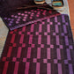 A dining table is set with two rectangular Halcyon Yarn Rep Weave Placemats featuring a gradient pattern of purples and reds in a geometric design. On the table are also two square dishes with a gradient from turquoise to brown, and a pair of chopsticks resting on one.