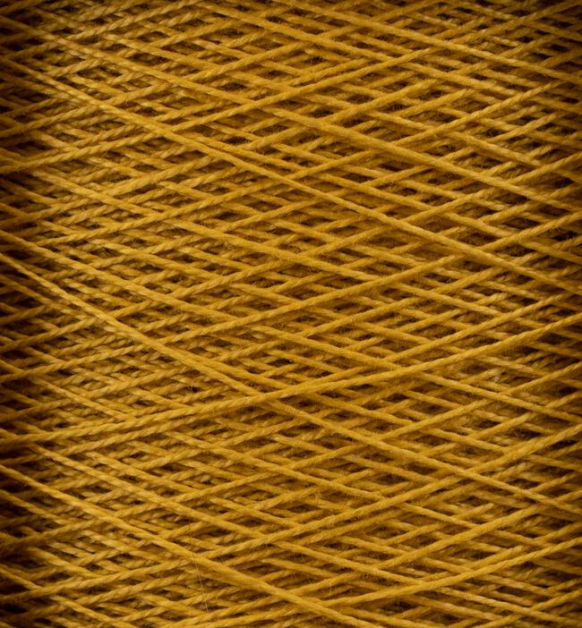 Close-up view of a spool of tightly wound, golden-yellow thread. The crisscross pattern of the 10/2 Pearl Cotton Yarn | Large Cone from Supreme Corp. is clearly visible, showcasing its texture and density. The color and detail highlight the thread's smooth, fibrous quality.