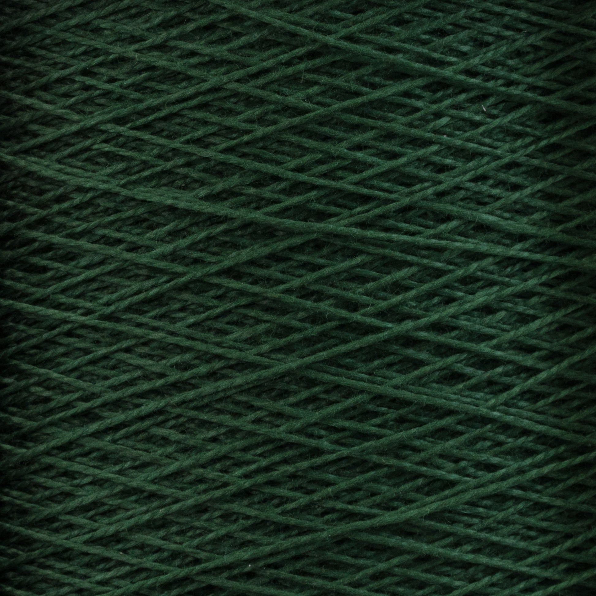 Close-up of Supreme Corp.'s 10/2 Pearl Cotton Yarn in a dark green hue, wound tightly in a criss-cross pattern. The fibrous texture and intricate overlap of threads are beautifully showcased. This colorfast yarn offers a rich, vibrant appearance, ideal for knitting or crochet projects with premium Pearl Cotton quality.