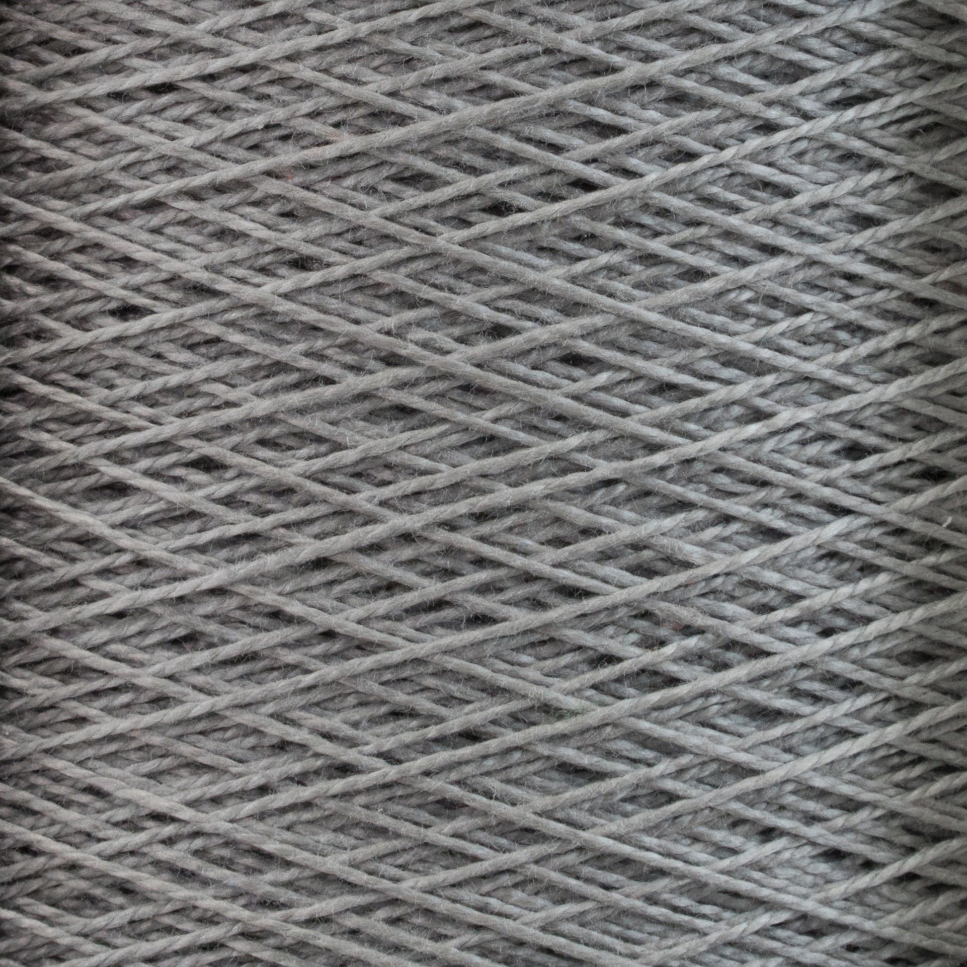 Close-up image of tightly wound grey 10/2 Pearl Cotton Yarn | Large Cone by Supreme Corp., showcasing the texture and intersecting threads.