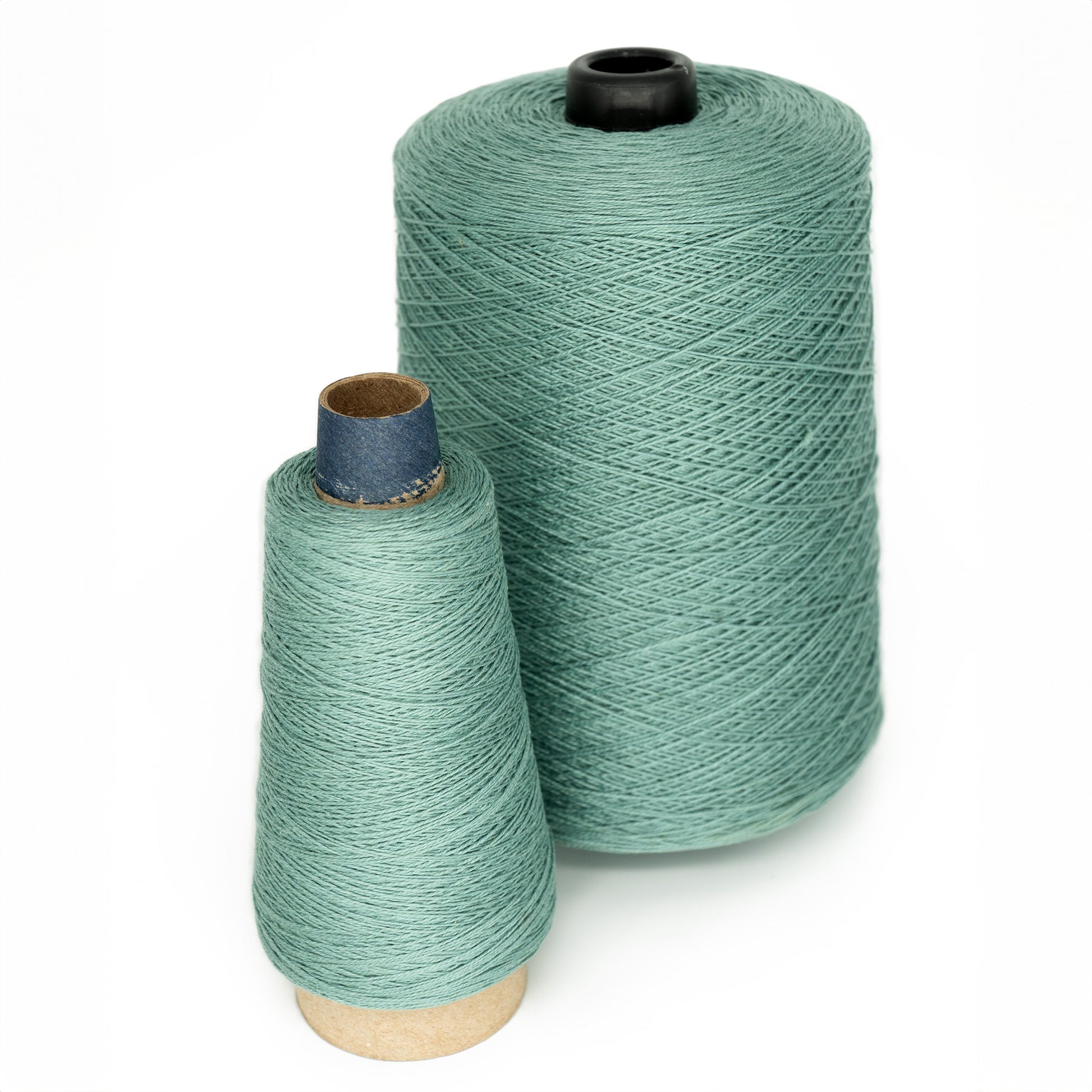 Two spools of teal-colored thread, crafted from colorfast Pearl Cotton, are displayed against a plain white background. The larger spool is the 10/2 Pearl Cotton Yarn | Large Cone by Supreme Corp., featuring cylindrical edges with black and white sections at the top and bottom. The smaller spool is also cylindrical but has a shorter blue inner core.