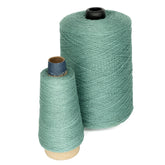 Two spools of Supreme Corp.'s 10/2 Pearl Cotton Yarn are displayed against a white background, highlighting their exceptional colorfastness. One is a large cone with a black core, and the other is smaller with a blue core. Both spools are tightly wound and feature a similar pastel green shade.