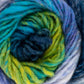 A close-up of a skein of Kureyon by Noro from Knitting Fever / Euro Yarns, showcasing a spiral of fibers in shades of blue, green, teal, and purple. The texture appears soft and fluffy, with gradual color changes blending seamlessly into one another.