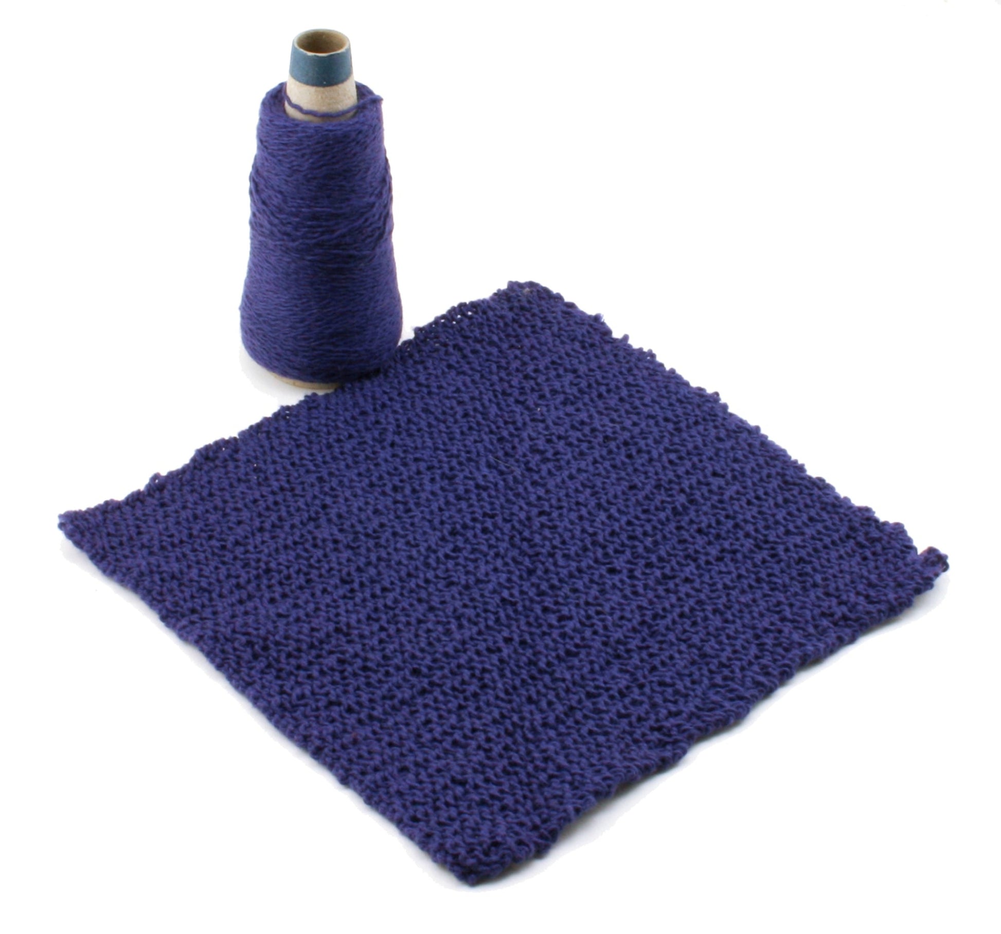 A purple knitted swatch lies flat on a white surface next to a matching spool of yarn from the Washcloths / Dishcloths Sampler by Halcyon Yarn. The square-shaped swatch features wash cloth patterns with a textured design. The tall spool has a paper core, and the yarn is tightly wound around it.