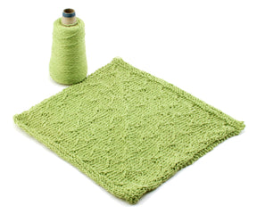 A cone of green Halcyon Yarn from the Washcloths / Dishcloths Sampler is positioned next to a green knitted cloth with a textured pattern, displayed on a white background. The yarn and the knit piece are the same shade of green, highlighting the connection between the material and the finished washcloth patterns—an ideal gift for any knitting enthusiast.