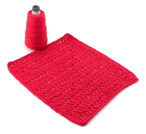 A rectangular, red, crocheted dishcloth from the Washcloths/Dishcloths Sampler by Halcyon Yarn laid flat next to a spool of matching Halcyon Yarn Casco Bay Sport in red. The dishcloth features small, evenly spaced holes and a textured surface, making it an ideal gift for anyone who appreciates handmade wash cloth patterns.