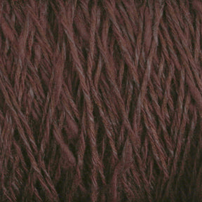 Close-up of a ball of yarn spun and dyed in Maine. The Halcyon Yarn Block Island Blend | Large Cone is dark maroon with a rich, textured appearance, showing the strands twisted together. The fibers look soft and slightly fuzzy, indicating a cozy material suitable for knitting or crocheting.