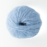 A ball of pale blue yarn from Plymouth Yarn Co., specifically their Plymouth Baby Alpaca Brush, sits against a white background. This soft, brushed alpaca yarn exhibits a fluffy and slightly fuzzy texture. Perfectly wound into a round shape, it’s ideal for versatile knitting or crocheting projects.