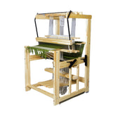 A Glimakra Julia 26", 4-Shaft Loom in a natural finish, with strands of white thread and an unfinished green woven cloth. The loom, branded by Glimakra, features multiple pedals and beams, designed to hold and adjust the threads for weaving. It is placed against a white background.