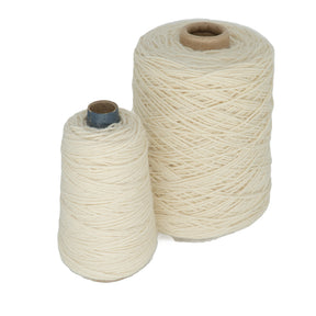 Two spools of cream-colored Jagger Brothers, Inc. Worsted Wool Warps are positioned side by side, echoing the style used in weft-faced projects. One spool is larger than the other, both featuring tightly wound fibers. The yarn appears soft and textured, making it ideal for knitting or crafting projects inspired by Navajo designs.