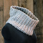 The Easy: Learn to Crochet Cowl by Halcyon Yarn, a light gray, hand-knit accessory featuring a textured pattern, is displayed on a black mannequin bust against a rustic wooden backdrop. Crafted with bulky weight yarn, this circular cowl looks cozy and soft, embodying detailed craftsmanship that makes it ideal for beginner crocheters.