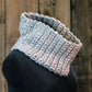 The "Easy: Learn to Crochet Cowl" by Halcyon Yarn, a hand-crocheted gray cowl scarf ideal for beginning crocheters, is displayed on a black mannequin against a wooden background. This scarf features a textured ribbed pattern made with bulky weight yarn, offering both cozy warmth and stylish appeal.