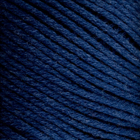 A close-up of Brown Sheep's Cotton Fleece in dark blue shows its tightly wound strands, creating a textured pattern. The slightly fuzzy yarn reveals individual fibers, highlighting the detailed texture perfect for intricate knitting patterns.