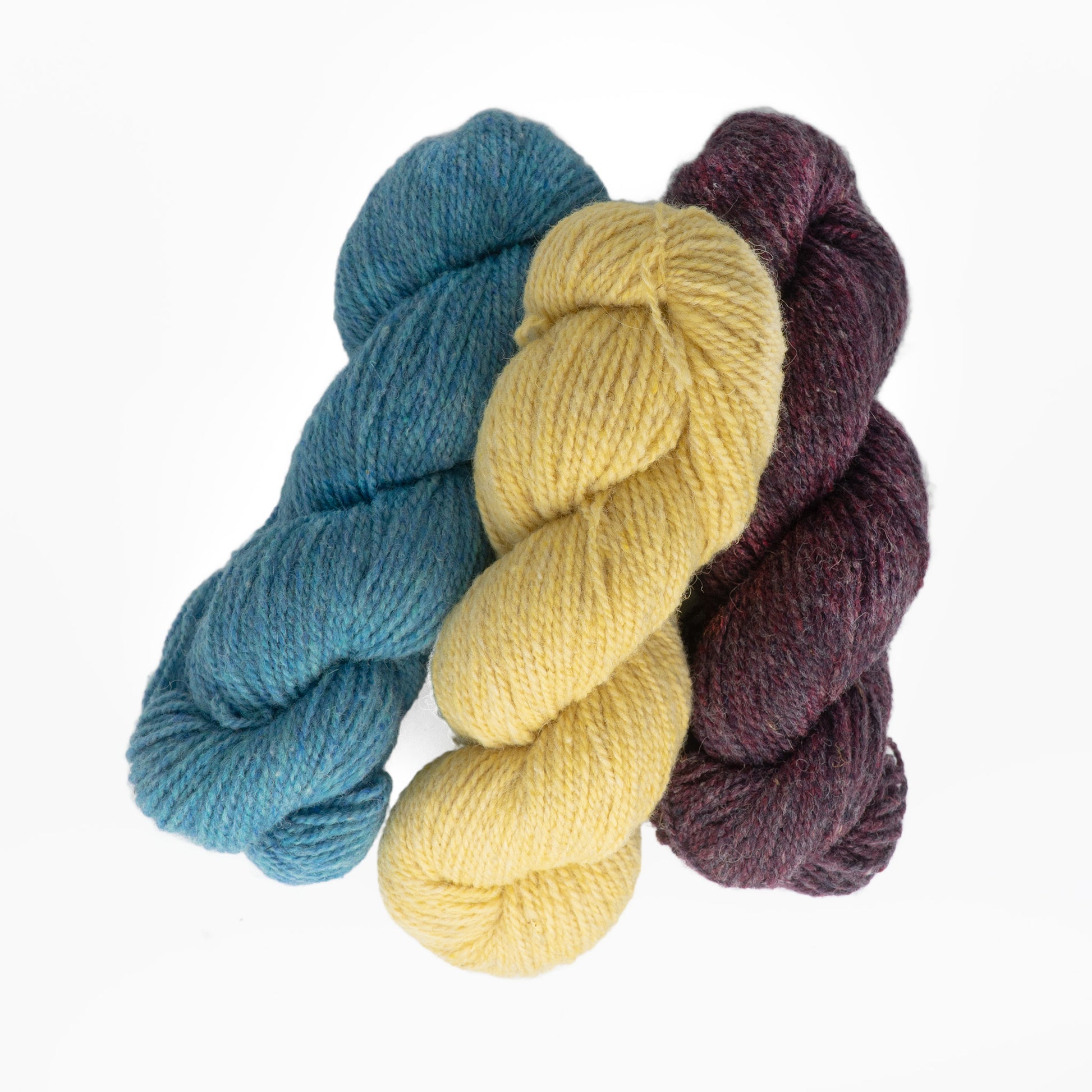 Three skeins of Bartlettyarns Maine Wool Yarn are shown against a white background. The yarn colors are teal-blue, yellow, and deep burgundy. The yarns are neatly twisted into classic skein shapes, and their textures appear soft and slightly fuzzy, highlighting the heathered colors of Bartlettyarns' Maine Wool.