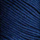 Close-up of Brown Sheep Cotton Fine, dark blue cotton yarn tightly wound into a ball. The texture of the yarn fibers is visible, showcasing a soft, slightly fuzzy surface perfect for machine knitters. The strands are neatly organized and evenly spaced.