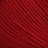 A close-up view of Brown Sheep's Cotton Fine yarn, showing the texture of the twisted threads. The red yarn appears soft and tightly wound, with slight variations in shading due to light reflections on the fibers, making it ideal for machine knitters.