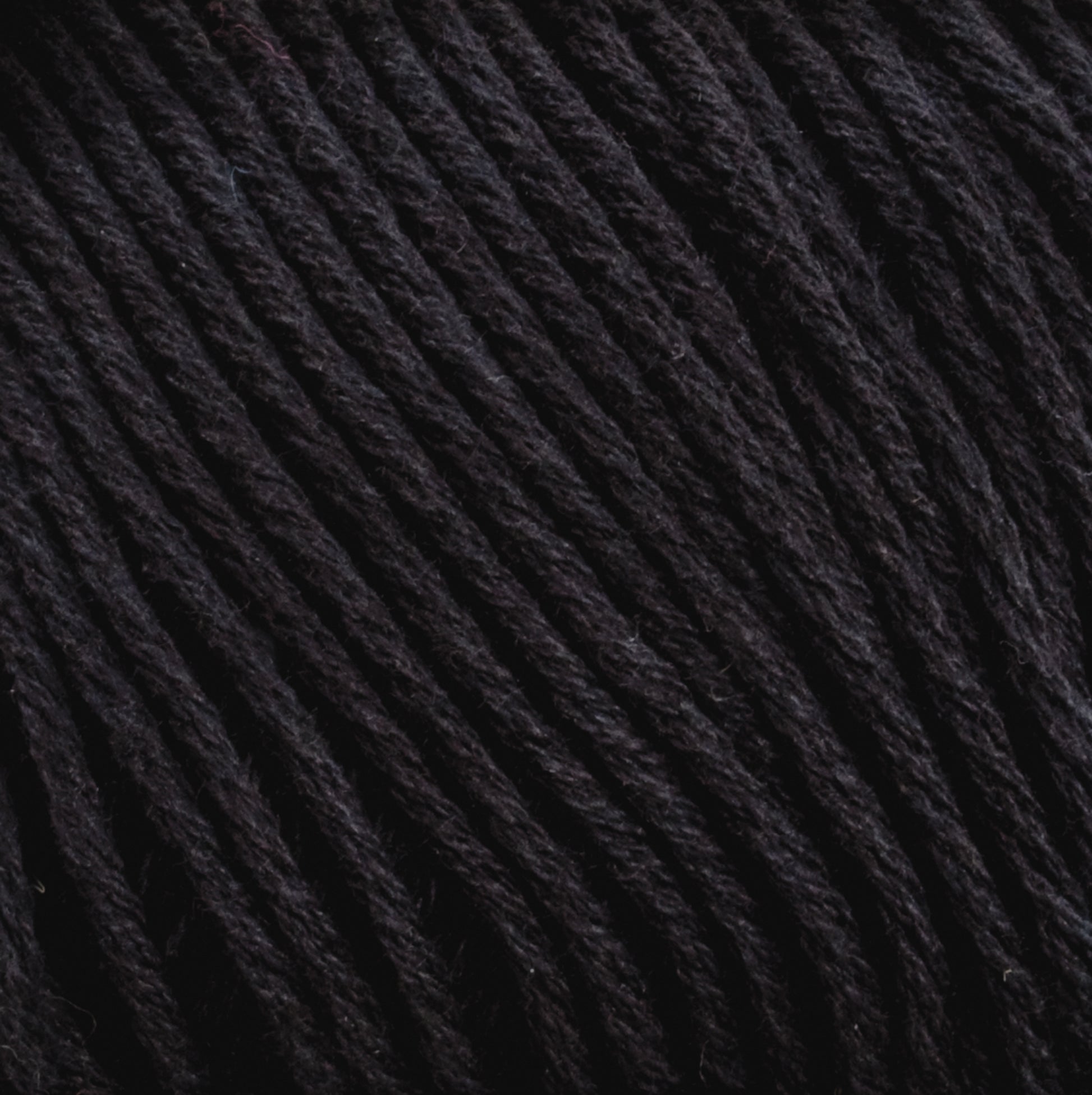 Close-up of Cotton Fine yarn by Brown Sheep. The image reveals tightly twisted black strands with a slightly glossy finish, suggesting it could be synthetic or a blend with natural fibers. The smooth texture makes it ideal for knitting, crocheting, or weaving projects for machine knitters.