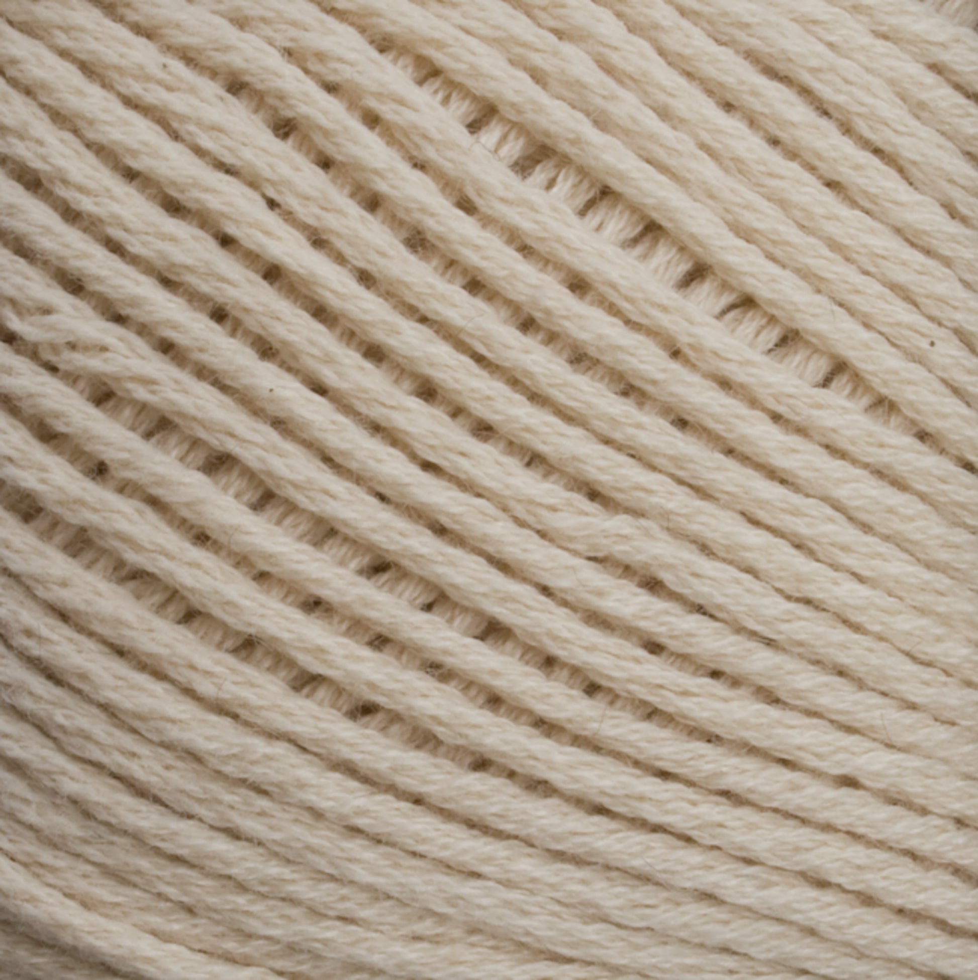 Close-up image of a ball of Cotton Fine yarn by Brown Sheep, showcasing the texture and tight weaving of the fibers. The yarn appears soft, with neatly arranged strands creating a diagonal pattern across the frame—a perfect choice for machine knitters.