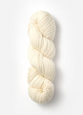 A single skein of Blue Sky Fibers Organic Cotton Worsted in off-white is coiled neatly against a plain white background. The texture of this worsted weight yarn from Blue Sky Fibers is soft, with a twisted appearance, making it perfect for baby knits or other knitting and crocheting projects.