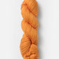 A skein of Blue Sky Fibers Organic Cotton Worsted yarn by Blue Sky Fibers is tightly wound in a spiral and displayed against a plain white background. The thick, orange yarn has a smooth, slightly glossy texture, and the fibers appear to be uniformly twisted together.