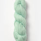 A skein of Blue Sky Fibers Organic Cotton Worsted yarn in mint green is coiled neatly against a plain white background. This yarn appears soft and thick, making it an excellent choice for knitting or crocheting projects, especially adorable baby knits.