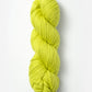 A twisted skein of Blue Sky Fibers Organic Cotton Worsted in a vibrant yellow-green hue, showcased against a plain white background. The yarn is thick, smooth, and appears soft, ideal for baby knits or other knitting or crocheting projects.