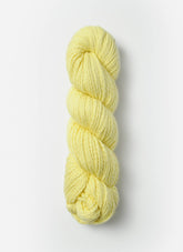 A skein of Blue Sky Fibers Organic Cotton Worsted, made from soft, pale yellow organic cotton yarn, tightly wound and twisted into a cylindrical shape, positioned vertically against a plain white background. The worsted weight yarn by Blue Sky Fibers appears thick and smooth, making it ideal for knitting or crocheting baby knits.