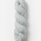 A neatly coiled skein of Blue Sky Fibers Organic Cotton Worsted yarn in light gray is displayed against a clean white background. The yarn, from Blue Sky Fibers, has a thick and chunky texture, making it suitable for knitting or crocheting projects that require bulky yarn, perfect for cozy baby knits.