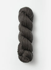 A skein of Blue Sky Fibers Organic Cotton Worsted in dark gray is displayed against a plain white background. This worsted weight yarn by Blue Sky Fibers, perfect for baby knits, is tightly twisted into a neat cylindrical shape.