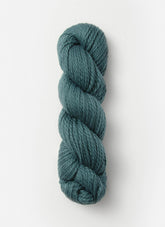 The Blue Sky Fibers Organic Cotton Worsted yarn in a beautiful teal color is neatly twisted into a loop. The fibers appear soft and slightly thick, making it ideal for knitting or crocheting cozy baby knits. The skein is set against a plain, light background with no additional objects in view.