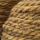 Close-up image of two balls of Cascade Eco and Cascade Eco Plus Wool Yarn by Cascade Yarns in a warm, golden-brown hue. The thick, slightly fuzzy texture of the yarn strands is visible, giving a sense of softness and warmth. The yarn is tightly wound, creating a layered, intertwined pattern perfect for felted knitting projects.