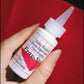 A hand holding a small white squeeze bottle with a pointed tip cap labeled "Fray-Stop" by Yarn Tree, showcasing usage instructions. Ideal for any weaver, it keeps your edges intact with its non-flammable formula that's safe for various materials. The background features red fabric.