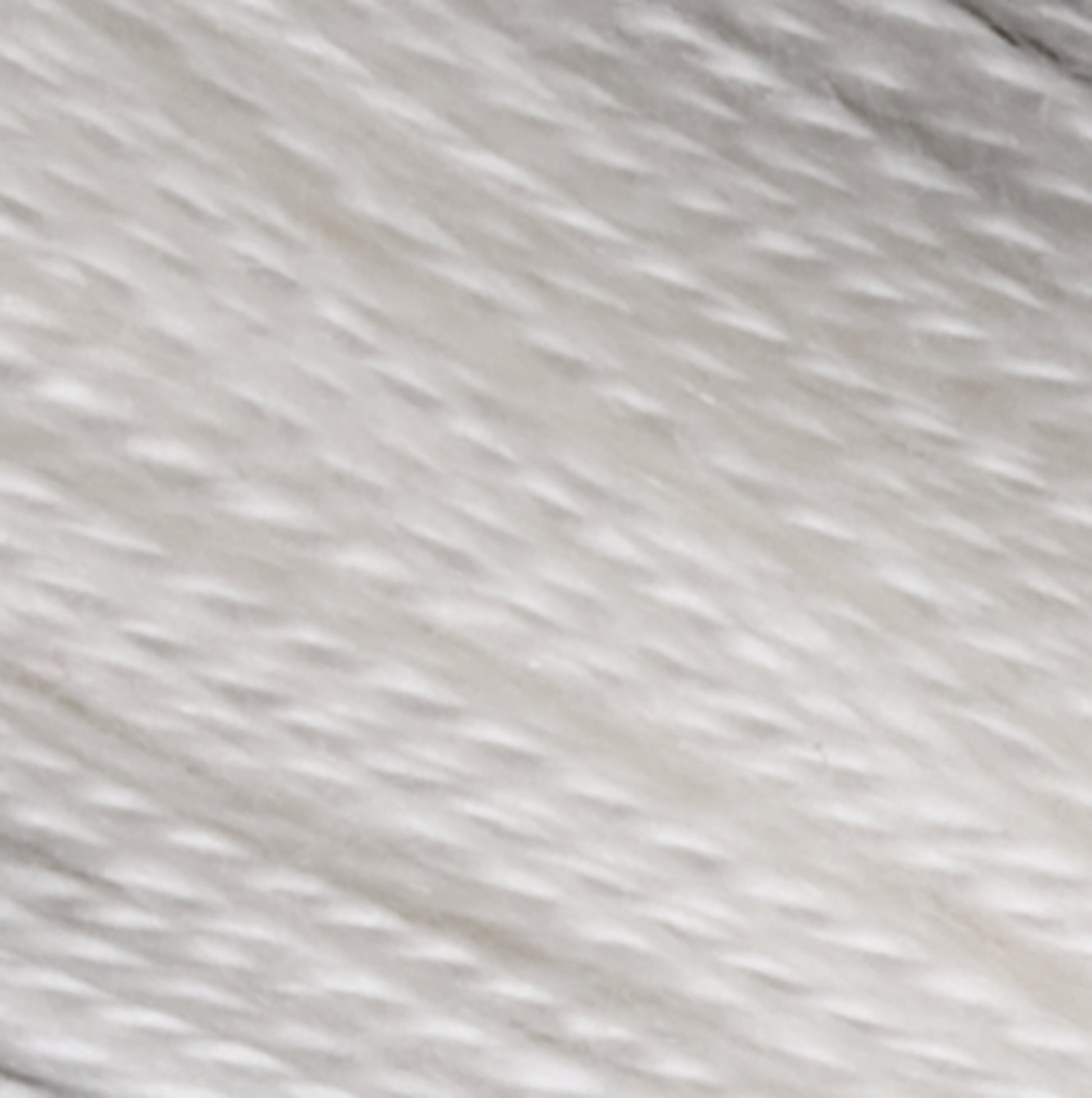 Close-up of the 2/30 Natural Silk Yarn from Henry's Attic, showcasing its soft texture with individual threads visible. The yarn appears smooth and slightly directional, creating a subtle pattern of fine lines reminiscent of delicate silk. The overall coloration is an even, bright white.