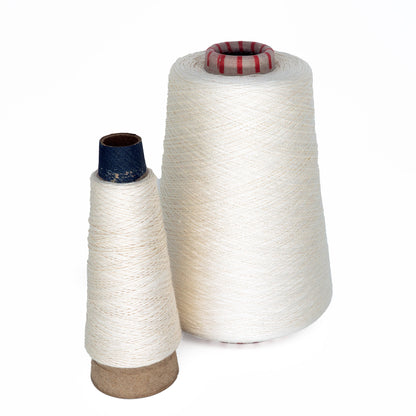 The white background highlights two mini-cones of undyed silk yarn, showcasing products from Henry's Attic. The larger cone features a red core, while the smaller one is finished with a blue core. Both cones are tightly wound, emphasizing their subtle texture and pristine natural color.