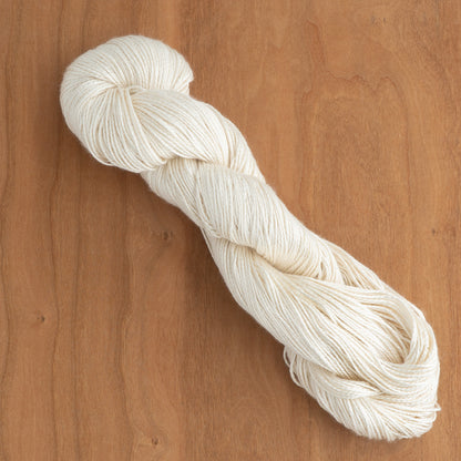 A neatly twisted skein of 2/5 Natural Silk Yarn by Henry's Attic lies on a light wooden surface. The yarn, smooth and well-arranged, highlights its texture and uniform off-white color—ideal for weaving. The wood's grain provides a warm contrast to the soft, creamy hue of the yarn.