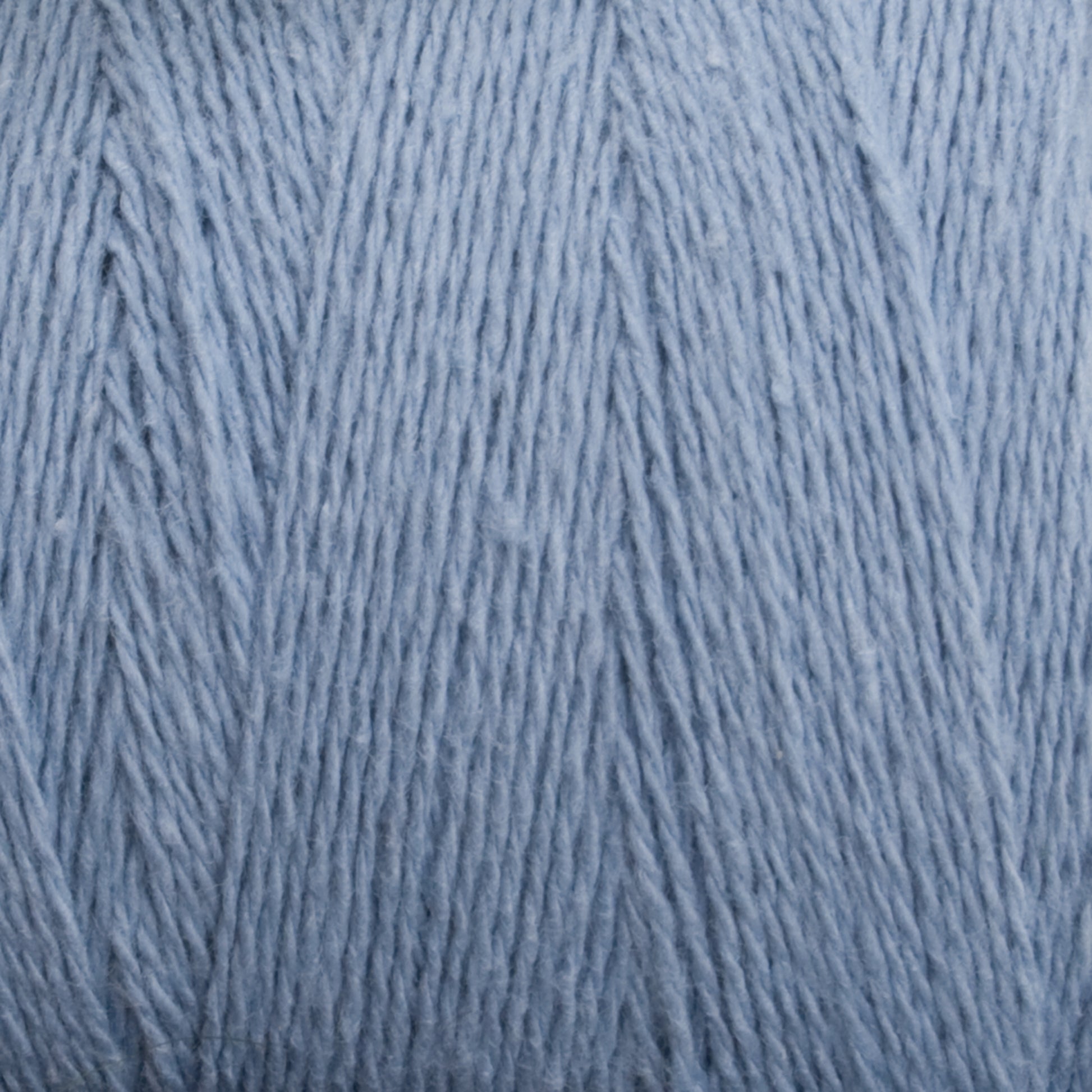 Close-up of a ball of Homestead 8/2 Cotton Yarn | Mini-cone by Supreme Corp in light blue, machine-washable yarn, showing the detailed texture of the fibers. The yarn is neatly wound, displaying a soft and smooth surface with fine strands intertwined together.