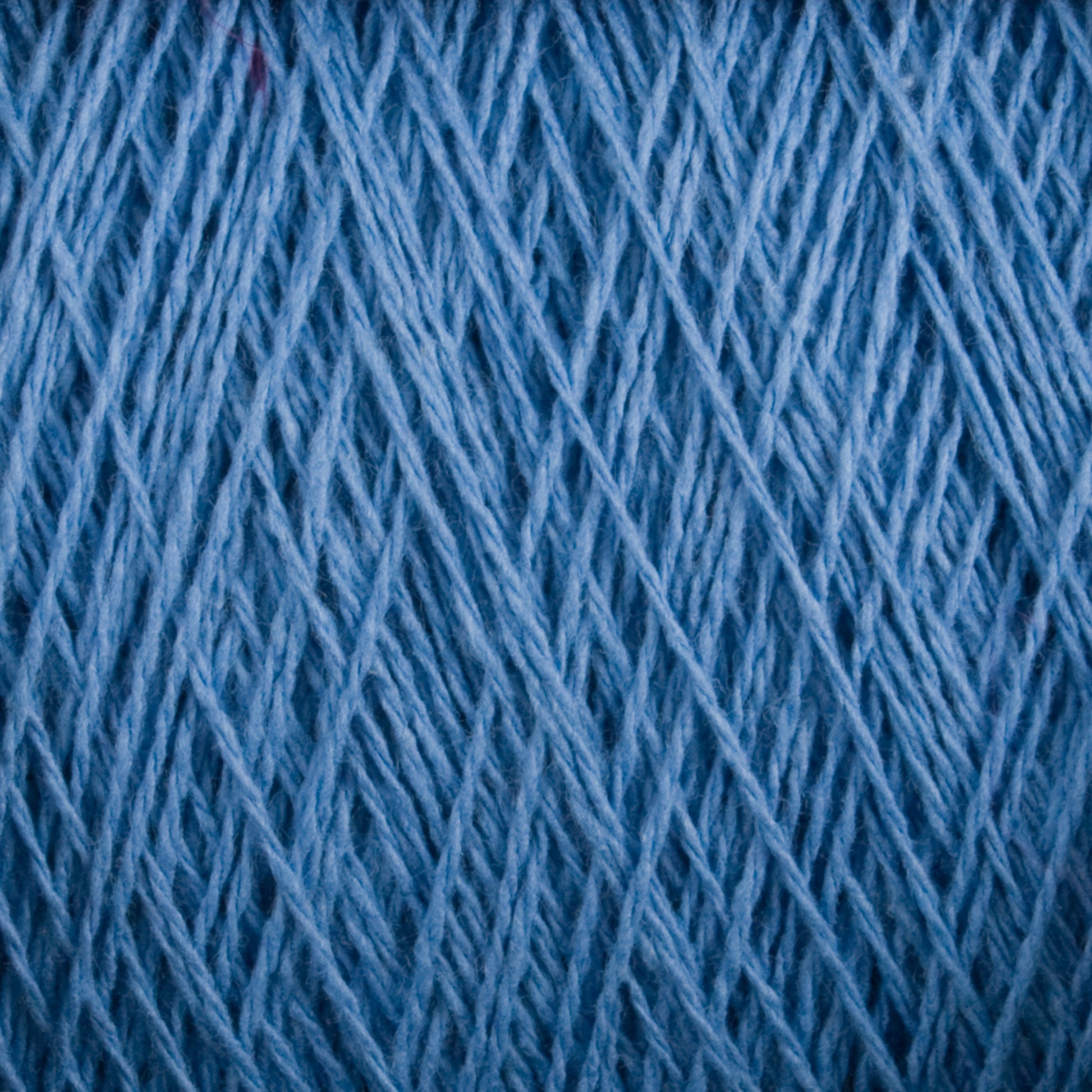 Close-up image of a spool of Supreme Corp's Homestead 8/2 Cotton Yarn in blue, showing its detailed woven fibers and texture. This machine-washable yarn appears tightly wound with a consistent thickness, making it ideal for all your weaving projects.